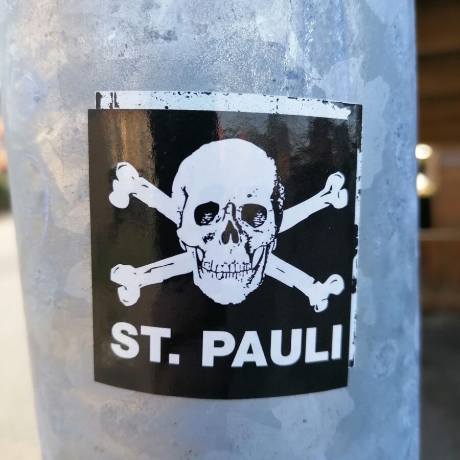 Aufkleber an einer Staßenlaterne: St. Pauli-Totenkopf-Logo mit Schriftzug "ST. PAULI".