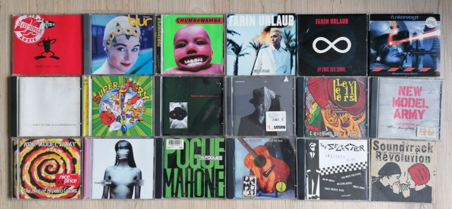 18 CDs liegen in drei Reihen auf dem Boden: - Die Ärzte - Schrei nach Liebe - Blur - Leisure - Chumbawamba - Tubthumper - Farin Urlaub - Endlich Urlaub! - Farin Urlaub - Am Ende der Sonne - Funker Vogt - Maschine Zeit - Fury In The Slaughterhouse - S/T - Fury In The Slaughterhouse - Super - Martin L. Gore - Counterfeit e.p - Peter Heppner - Solo - The Levellers - Levelling The Land - New Model Army - History (The Singles 85-91) - New Model Army - The Love Of Hopeless Causes - Placebo - Meds - The Pogues - Pogue Mahone - The Pogues - The Rest Of The Best - The Selecter - Greatest Hits - Soundtrack zur sozialen Revolution